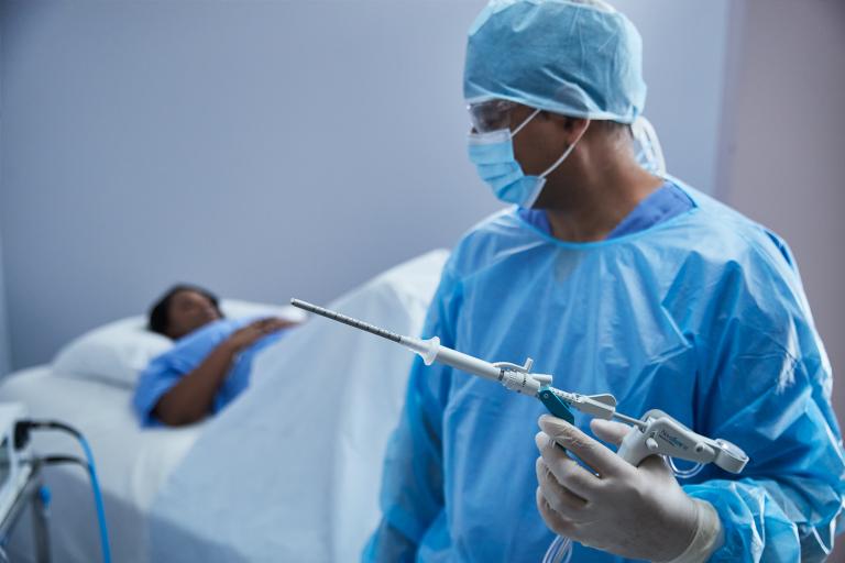 Chirurgo che tiene in mano un dispositivo medico con una paziente su un letto d'ospedale sullo sfondo