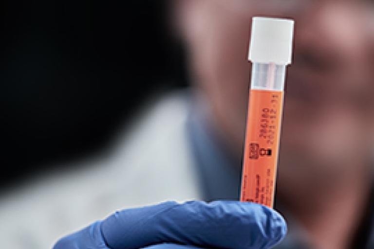 Mano con guanto che tiene una provetta