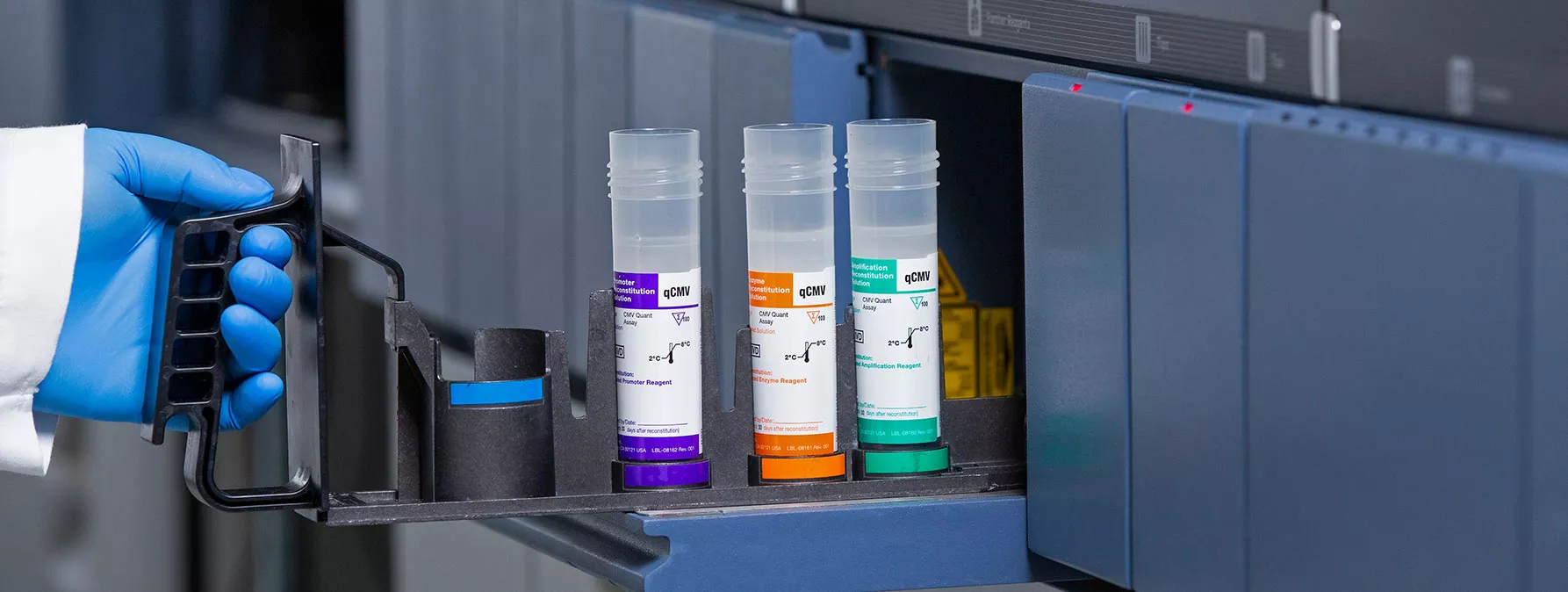 Gloved hand putting tray of Vials into equipment in lab setting