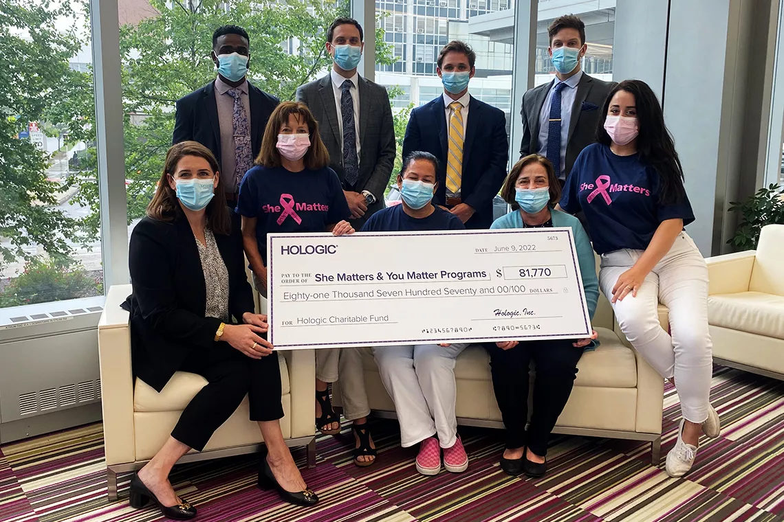 Foto di gruppo di persone mascherate che tengono un grande assegno promozionale a sostegno dei programmi She Matters e You Matter